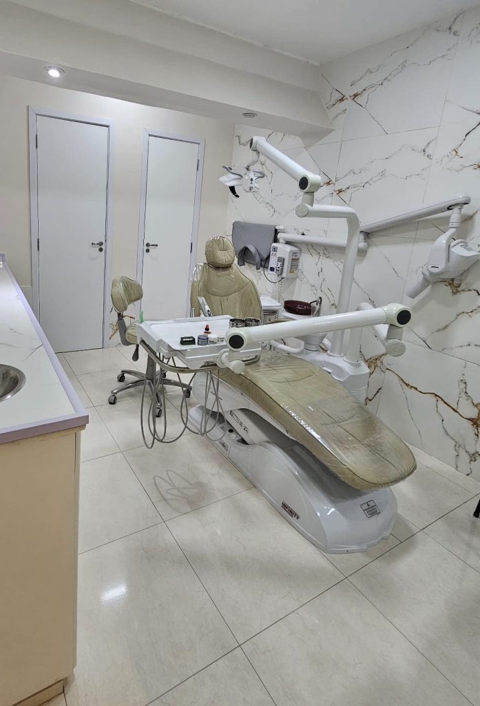 Interior do consultório odontológico moderno da Dra. Amanda Magre no Alto da Boa Vista, RJ, mostrando a cadeira de dentista bege, microscópio cirúrgico dental de braço longo e paredes de mármore.